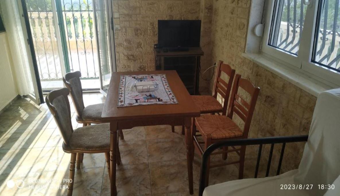 A dining area with a table and chairs, a television on a stand, and a window with a view of the outside.
