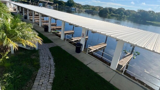 Un hotel frente al mar con un paseo techado, palmeras y vistas al agua.