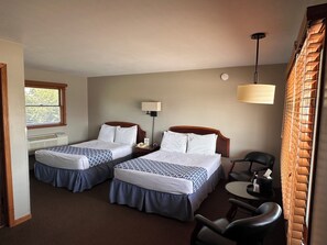 A hotel room with two beds, a desk, a chair, a lamp, and a window with blinds. - Grant Hills Motel (Galena)