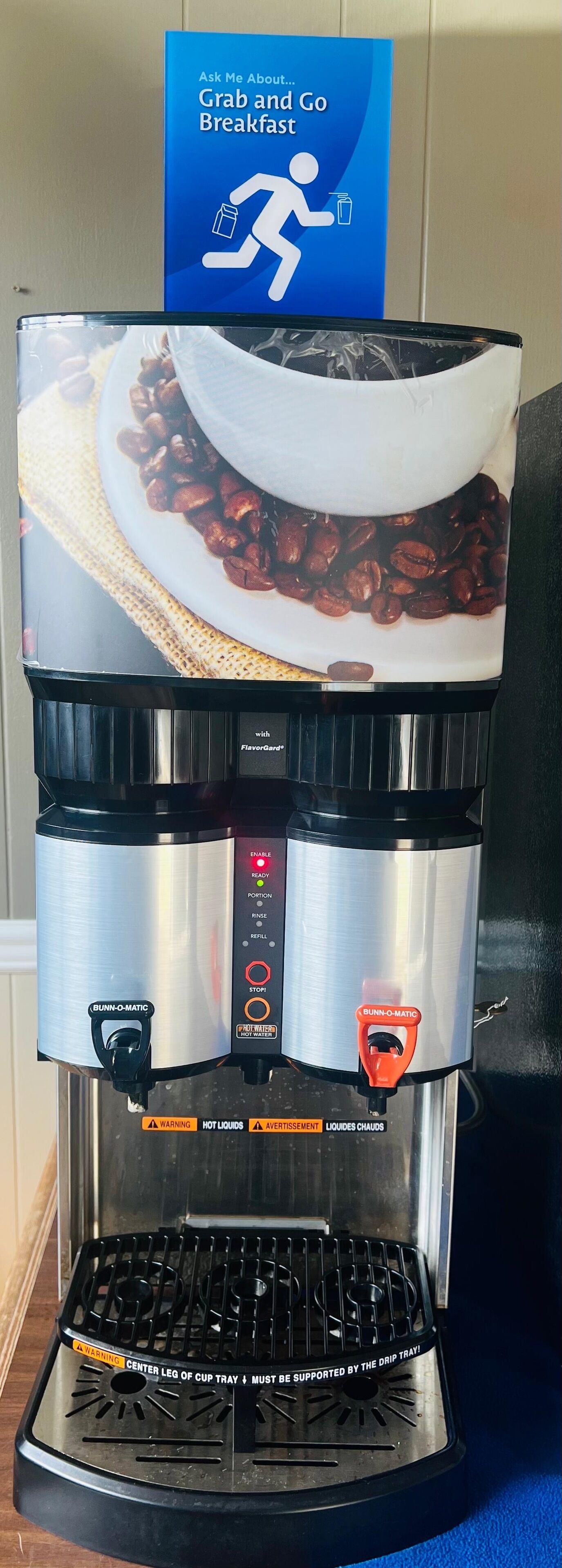 Une machine à café dotée d’un bac de récupération, d’un panneau de commande et d’un motif représentant une tasse de café.