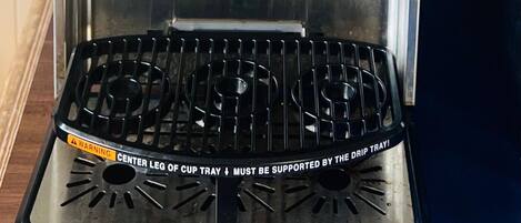Une machine à café dotée d’un bac de récupération, d’un panneau de commande et d’un motif représentant une tasse de café.