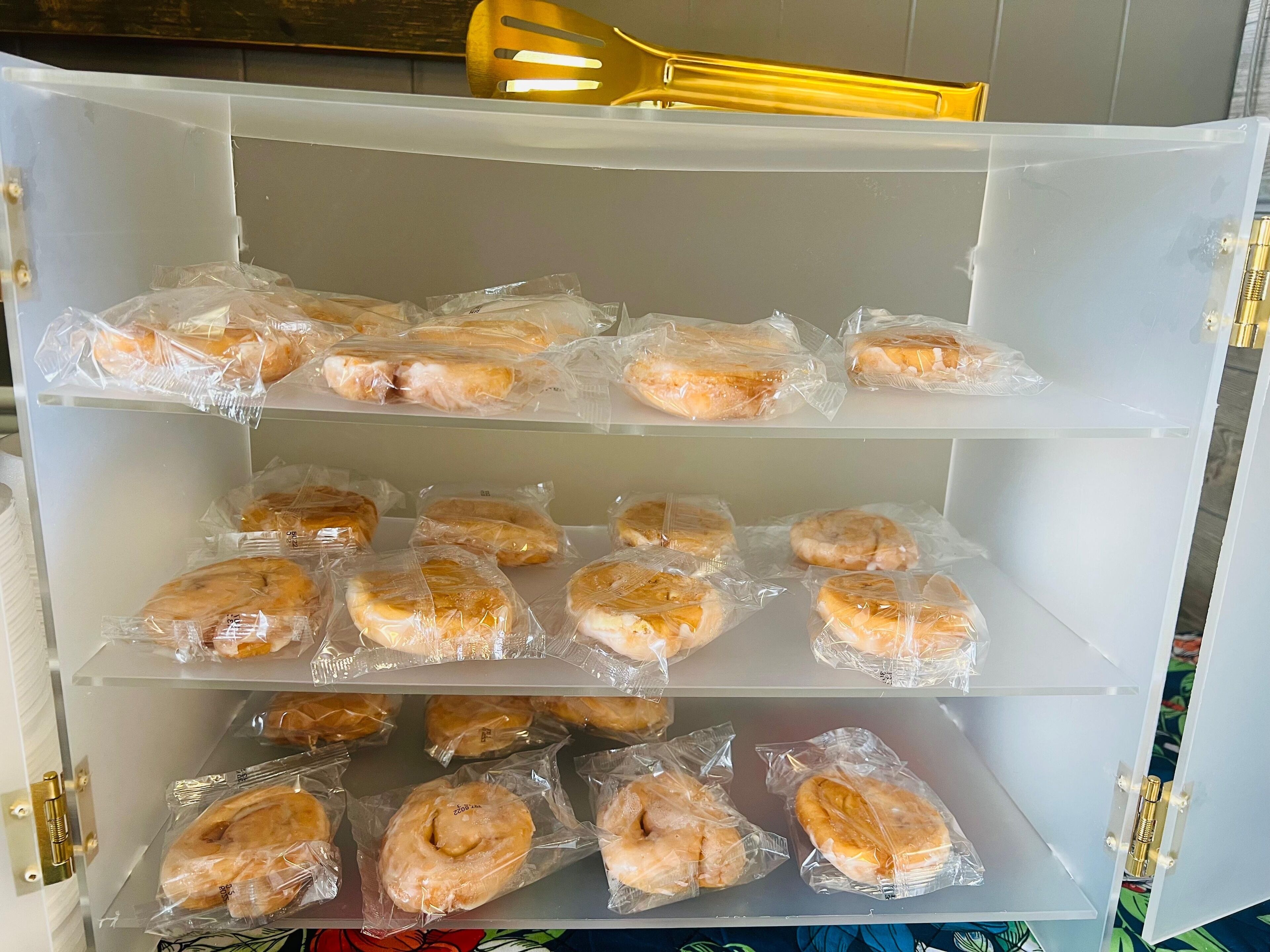 Ett förvaringsskåp med flera hyllor där bakverk, inlindade i plast, förvaras.