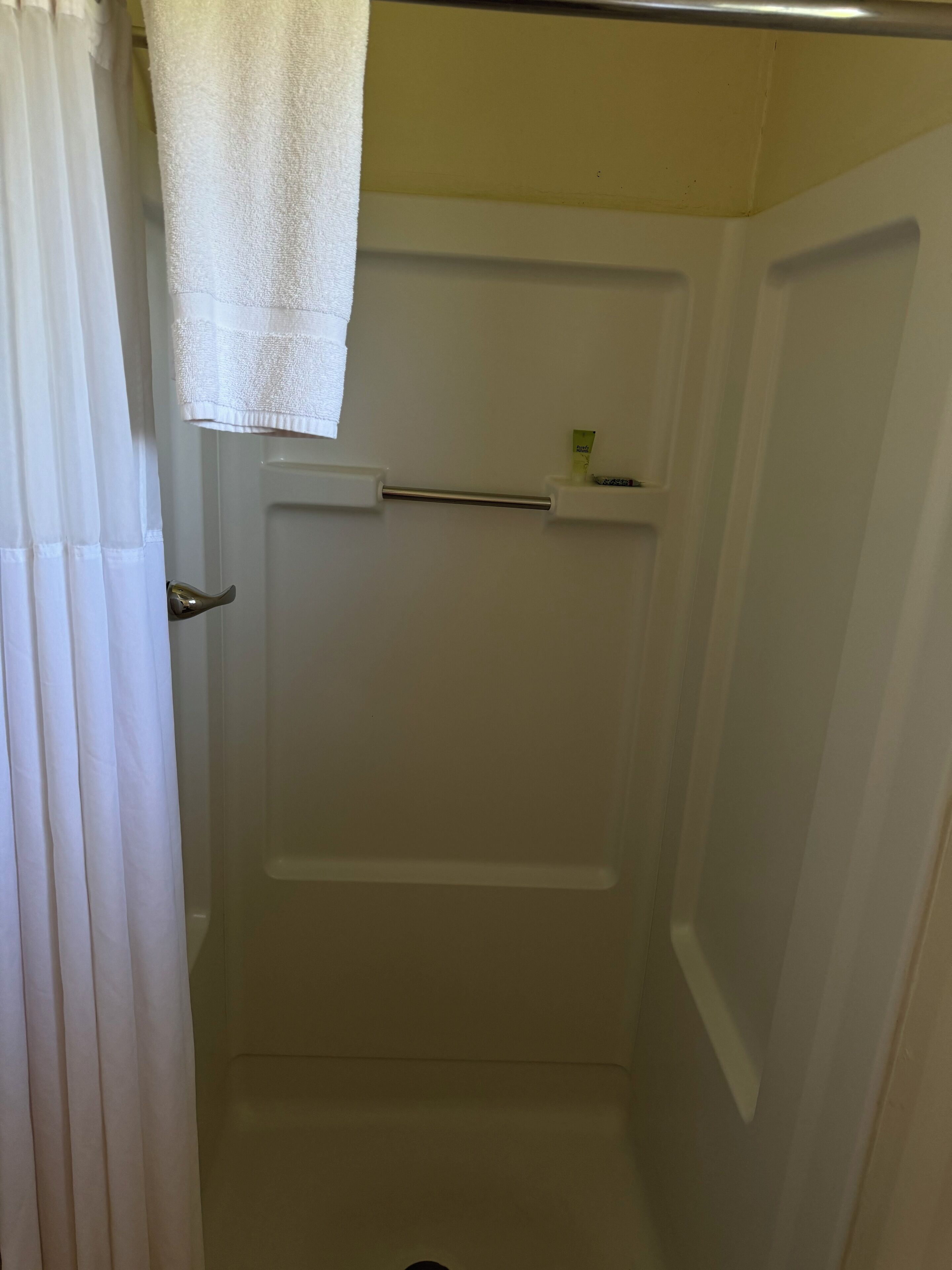 A bathroom with a shower, a towel rack, and a small shelf with toiletries.