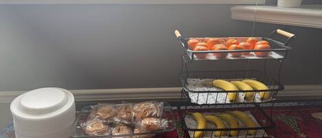 A kitchen counter with a fruit basket containing oranges and bananas, a stack of white plates, and a glass container.