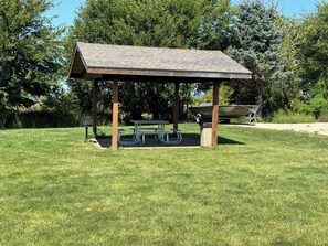 A covered picnic area with a table and benches, surrounded by grass and trees. - Grant Hills Motel (Galena)