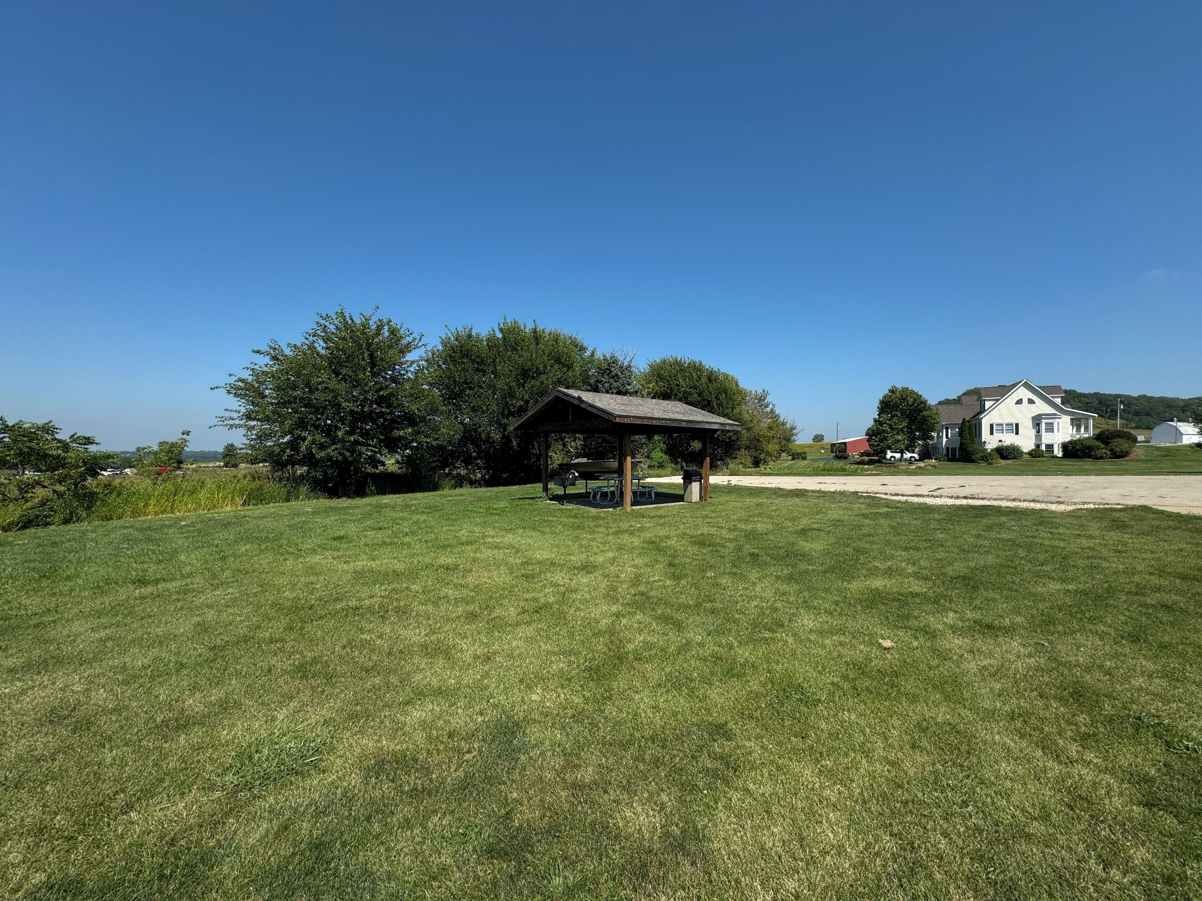 Een grasveld met een houten paviljoen, een wit huis en een schuur op de achtergrond.