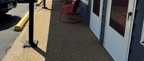 A covered outdoor seating area with rows of red chairs and a gravel floor, adjacent to a building with numbered doors.