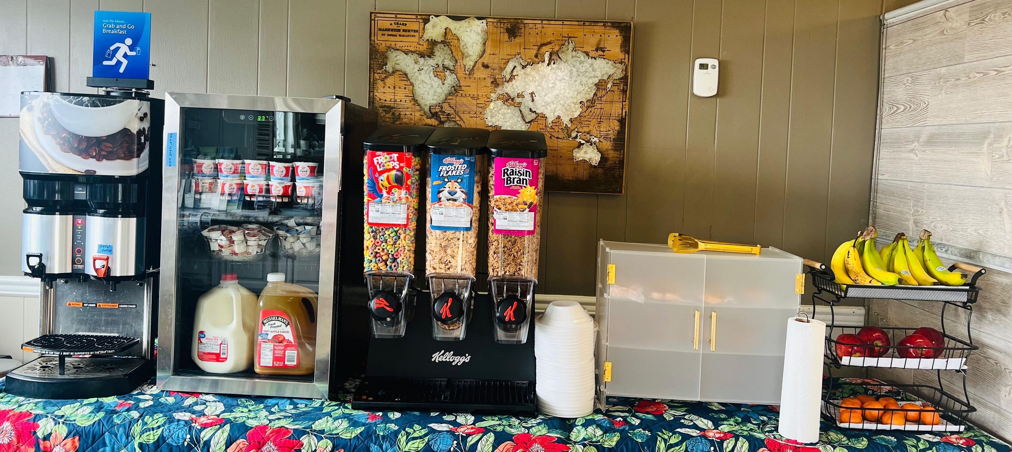 Estação de pequeno-almoço com máquina de café, dispensador de leite, dispensador de cereais e exposição de fruta.