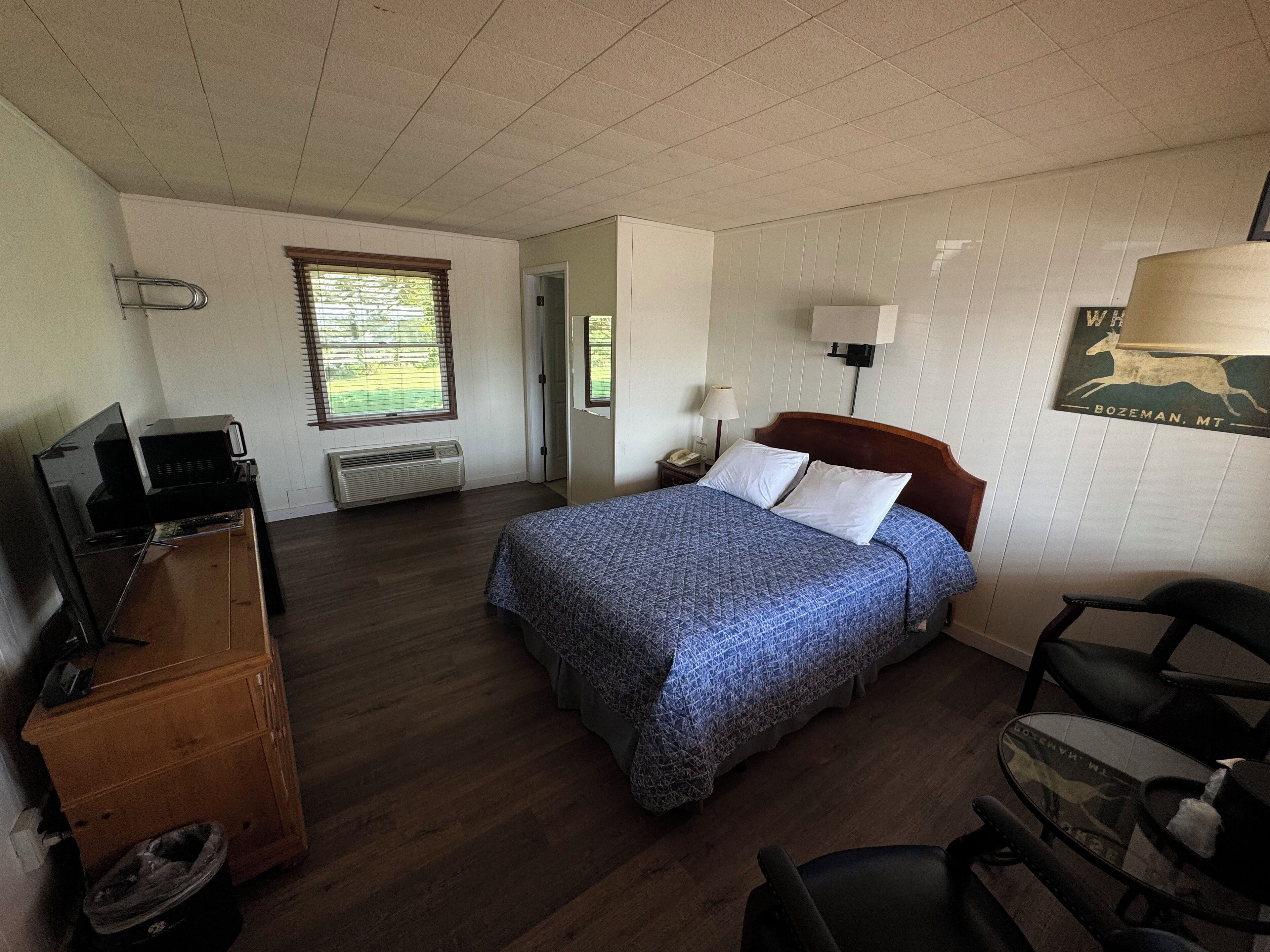 Un dormitorio con una cama, un escritorio con computadora, una silla, una lámpara y un cuadro en la pared.