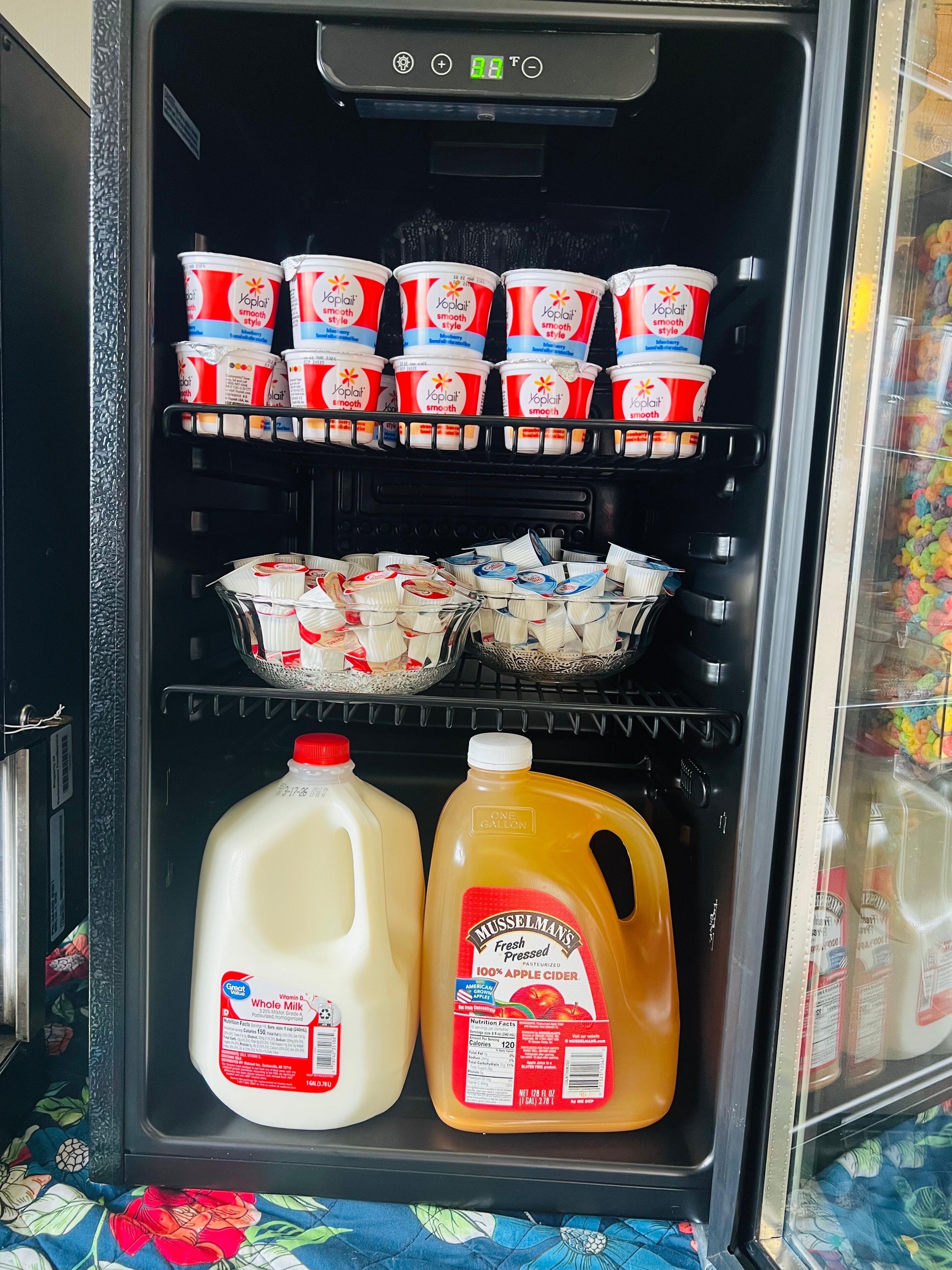 A refrigerator with multiple shelves containing various food items, including yogurt cups, milk cartons, and a large jug of apple cider.