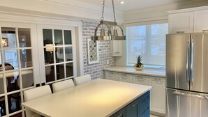 A kitchen with white cabinetry, a stainless steel refrigerator, and a dining area with a white table and chairs.