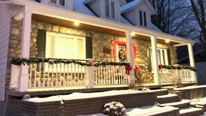 A two-story house with a stone facade, a porch with a white railing, and snow on the ground.