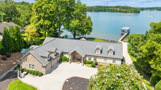 Une grande maison à l’extérieur en pierre, dotée d’une allée spacieuse et entourée d’une végétation luxuriante, avec vue sur un lac.