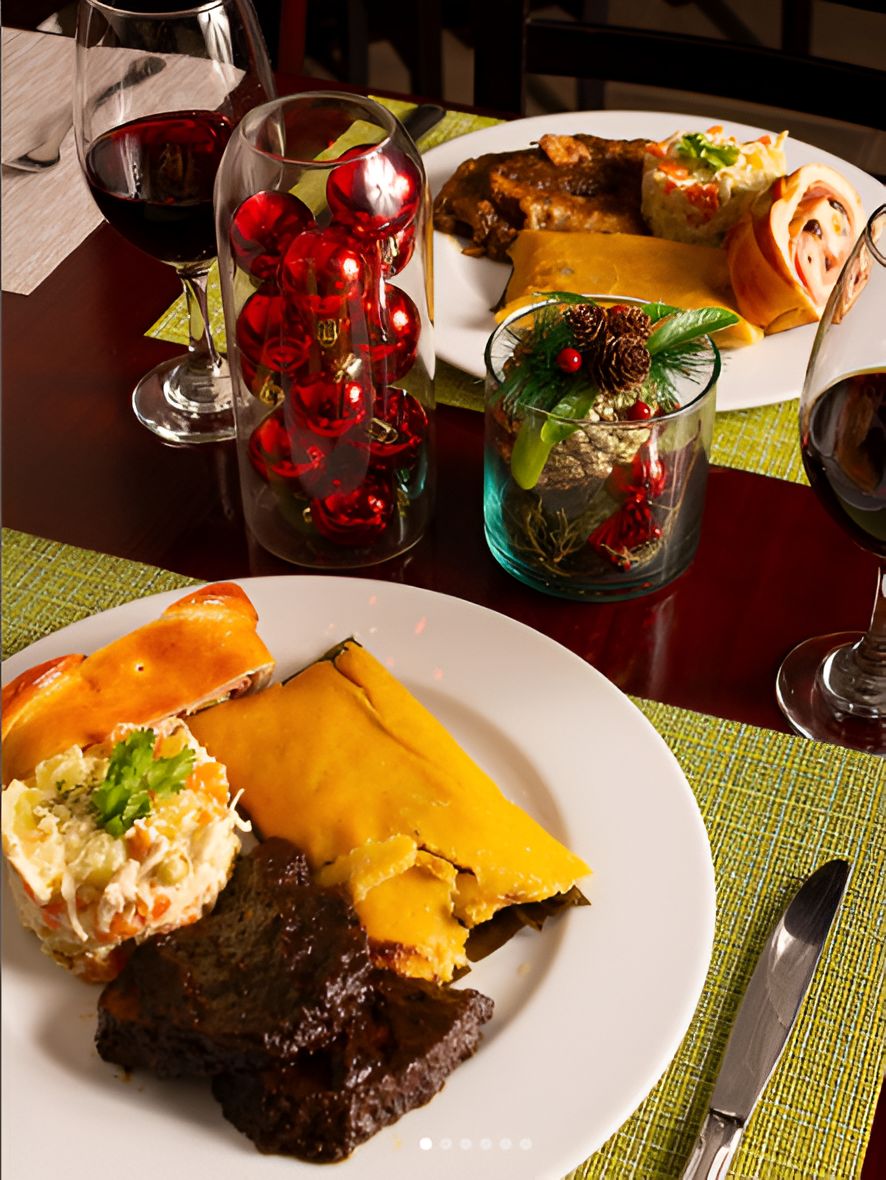A dining table with a plate of food, a glass of red wine, and a decorative glass with red ornaments.