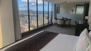 A hotel room with a large bed, a dining area with a table and chairs, and a view of the cityscape through large windows. - Hotel Chacao Suites (Caracas)