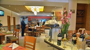 A restaurant with tables set for dining, a bar area with bottles, and a decorative orchid arrangement. - Hotel Chacao Suites (Caracas)