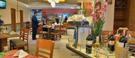 A restaurant with tables set for dining, a bar area with bottles, and a decorative orchid arrangement.