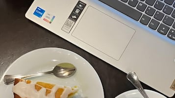 Een laptop, een bord met een stukje taart, een lepel en een kop koffie op een tafel.