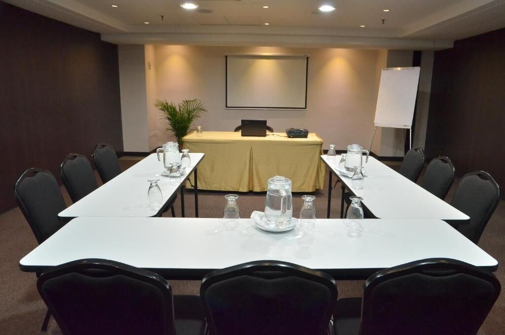 A conference room with a long table, chairs, a laptop, a projector screen, and a whiteboard.