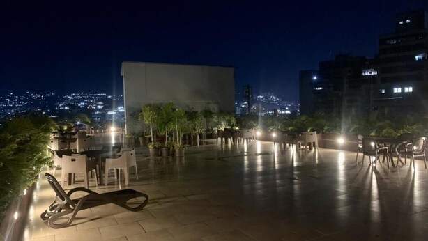 An outdoor terrace with seating and potted plants, overlooking a cityscape at night. - Hotel Chacao Suites (Caracas)