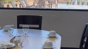 Een eettafel gedekt met borden, glazen en bestek, met uitzicht op een stadsbeeld en groen door grote ramen.