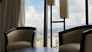 A modern room with two leather armchairs, a round table, and floor lamps. Large windows offer a city view. - Hotel Chacao Suites (Caracas)