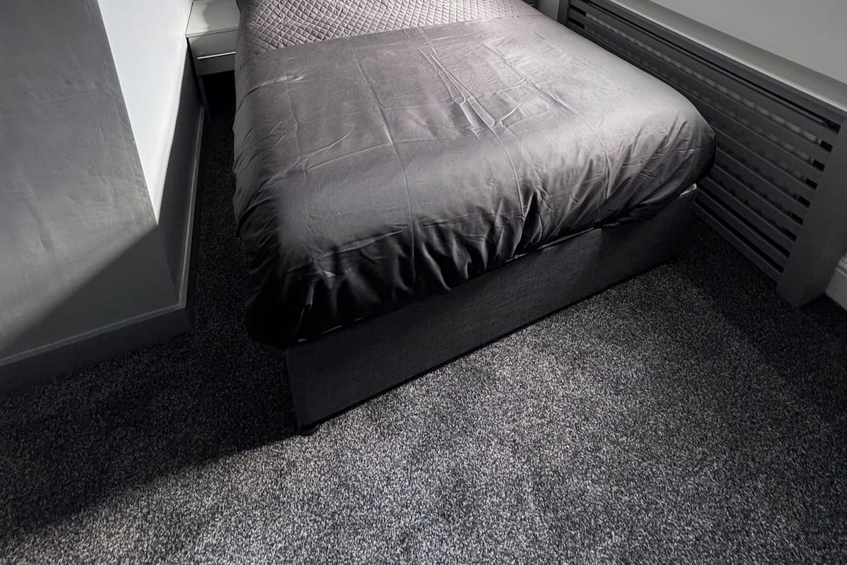 A small, modern bedroom with a single bed, a window, and a radiator.