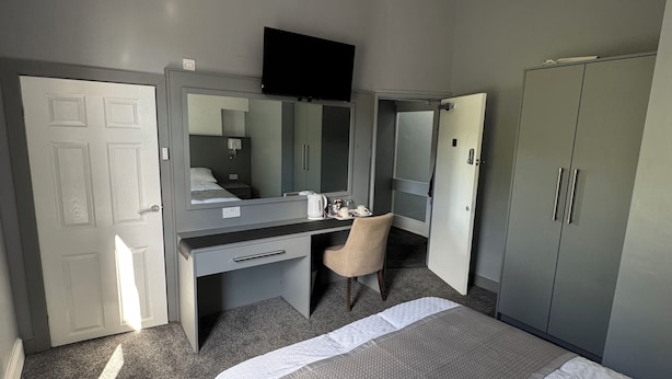 A hotel room with a bed, a desk with a chair, a wardrobe, and a television on the wall. - Waverley park house (Preston)