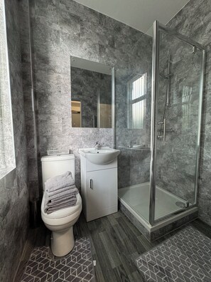 A modern bathroom with a toilet, sink, and glass-enclosed shower. - Waverley park house (Preston)