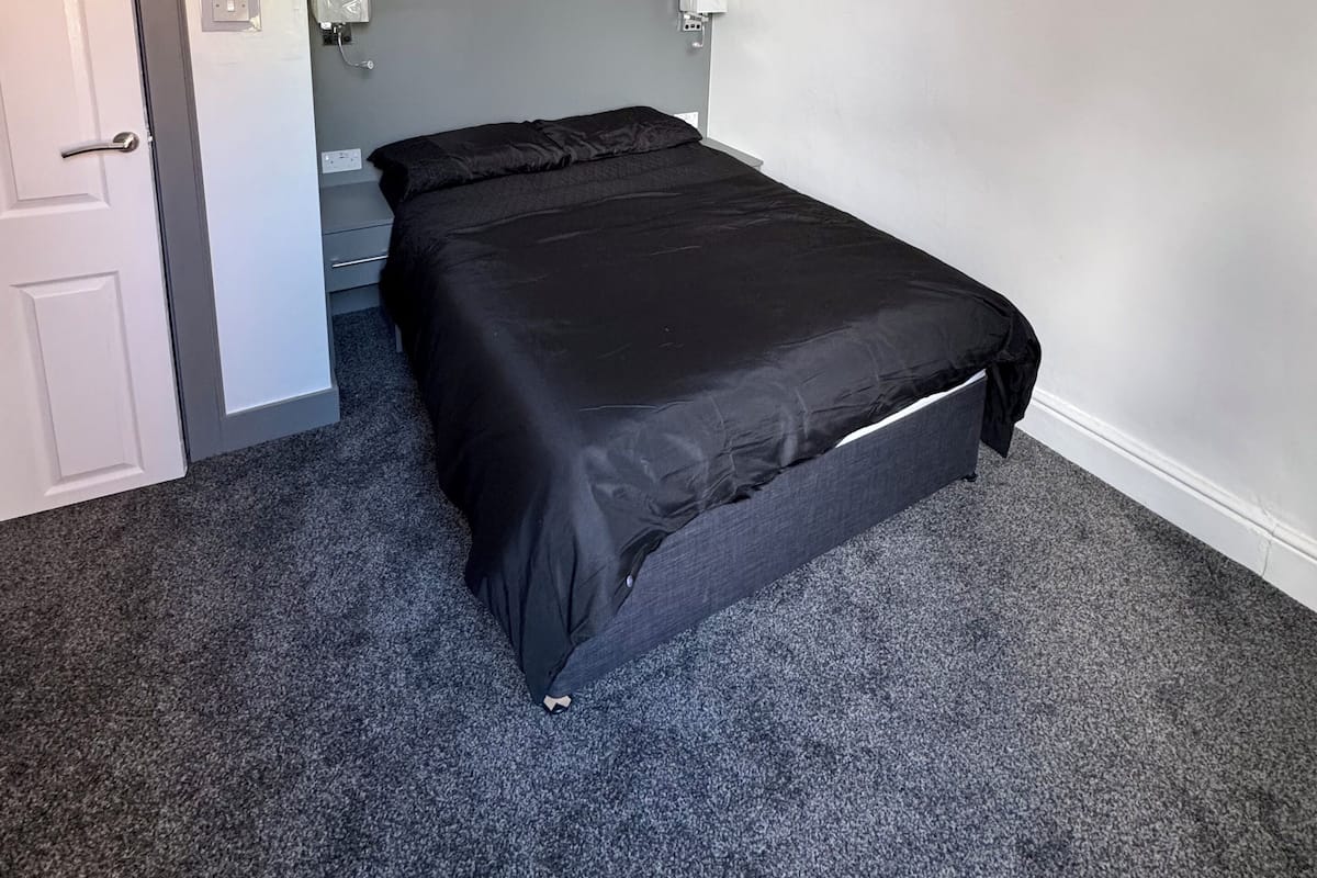 A bedroom with a bed, a door, a light switch, and a ceiling light fixture.