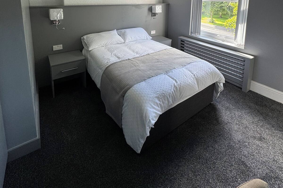 A bedroom with a bed, nightstands, a window with a view, and a ceiling light.