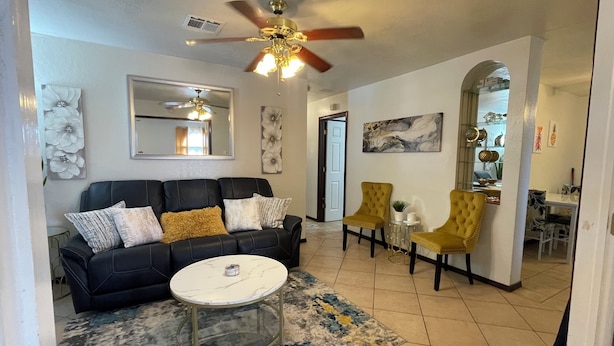 A living room with a black leather sofa, a round coffee table, and two yellow armchairs. There is a ceiling fan, a mirror, and a painting on the wall. - Lawton/Fort Sill Home near Airport  (Lawton)