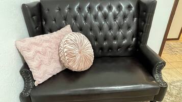 En sort lædersofa med buet ryg og armlæn, to dekorative puder og en blød måtte.