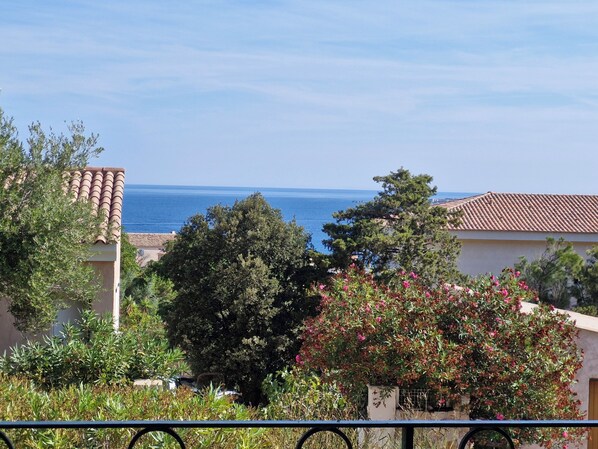A coastal residential area with terracotta-roofed buildings, lush greenery, and a clear view of the sea.