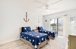 Ein Schlafzimmer mit zwei Betten, einem Deckenventilator, einer Schiebetür zu einem Balkon und einem Schild an der Wand.