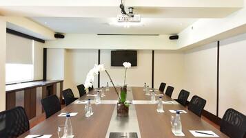 A conference room with a long table, chairs, a projector, and a screen.