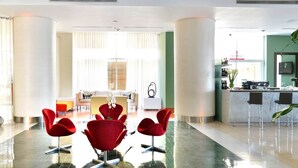 A modern hotel lobby with a reception desk, red chairs, a sofa, and a dining area. - Hotel Pestana Caracas Premium (Caracas)
