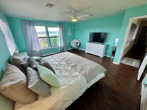 A bedroom with a large bed, a television, a dresser, and a window with curtains. - Sunset Cove Lakehouse 4-bed plus loft Waterfront Closest to the Boat Ramp - Park (Lago Vista)