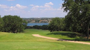 Campo de golf con vista despejada a un cuerpo de agua y edificios a lo lejos.