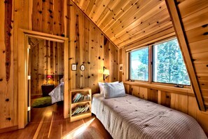 Quarto de cabana de madeira com uma cama, uma mesa de cabeceira, um abajur e uma estante de livros.