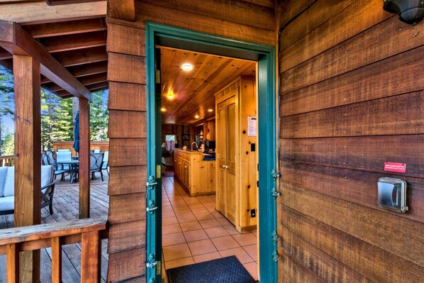 Una cabaña de madera con un área de estar exterior cubierta y una cocina con armarios de madera y piso de baldosas.