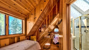 A wooden cabin interior with a bed, a small desk, a window with a view of trees, and a glass shower enclosure. - Cedar Flat - Views of the Lake! (Carnelian Bay)