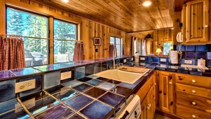 A wooden cabin with a kitchen featuring a large window, a sink, and wooden cabinets. - Cedar Flat - Views of the Lake! (Carnelian Bay)