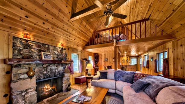 A cozy cabin interior with a stone fireplace, wooden ceiling, and a large sofa. - Cedar Flat - Views of the Lake! (Carnelian Bay)