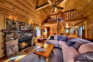 Interior acogedor de una cabaña con chimenea de piedra, techo de madera y un sofá grande.