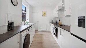 A modern kitchen with white cabinetry, a built-in washing machine, a water dispenser, and a clock on the wall.