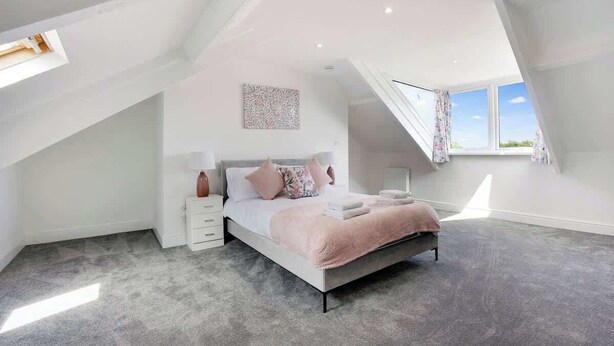 A bedroom with a sloped ceiling, a bed with pillows and a blanket, a nightstand, and a window with curtains.