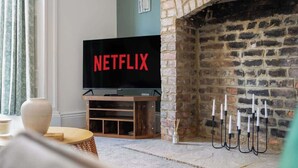 A living room with a TV displaying 'NETFLIX,' a fireplace, and a stone wall.