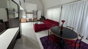 A modern living room with a red sofa, a dining table with chairs, and a staircase leading to a loft area. - Hotel Cuarta Avenida (Caracas)