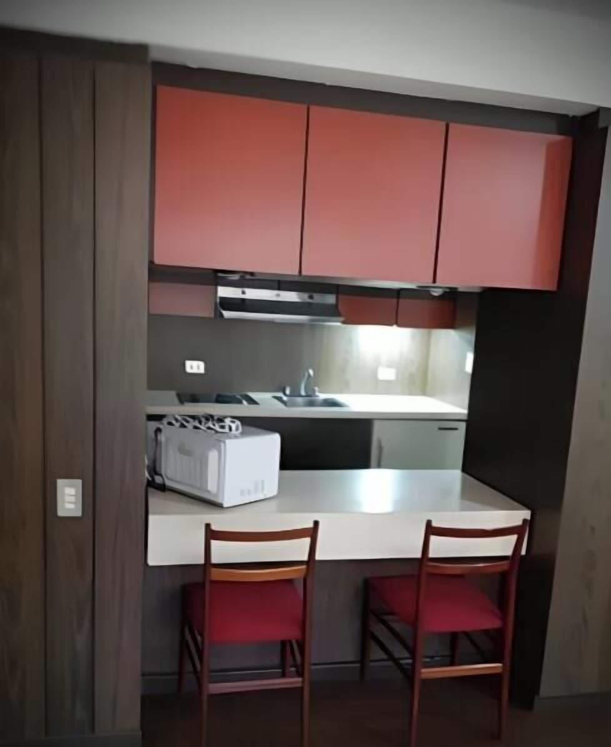 Une cuisine de taille réduite avec des meubles rouges, un plan de travail blanc et deux chaises en bois.